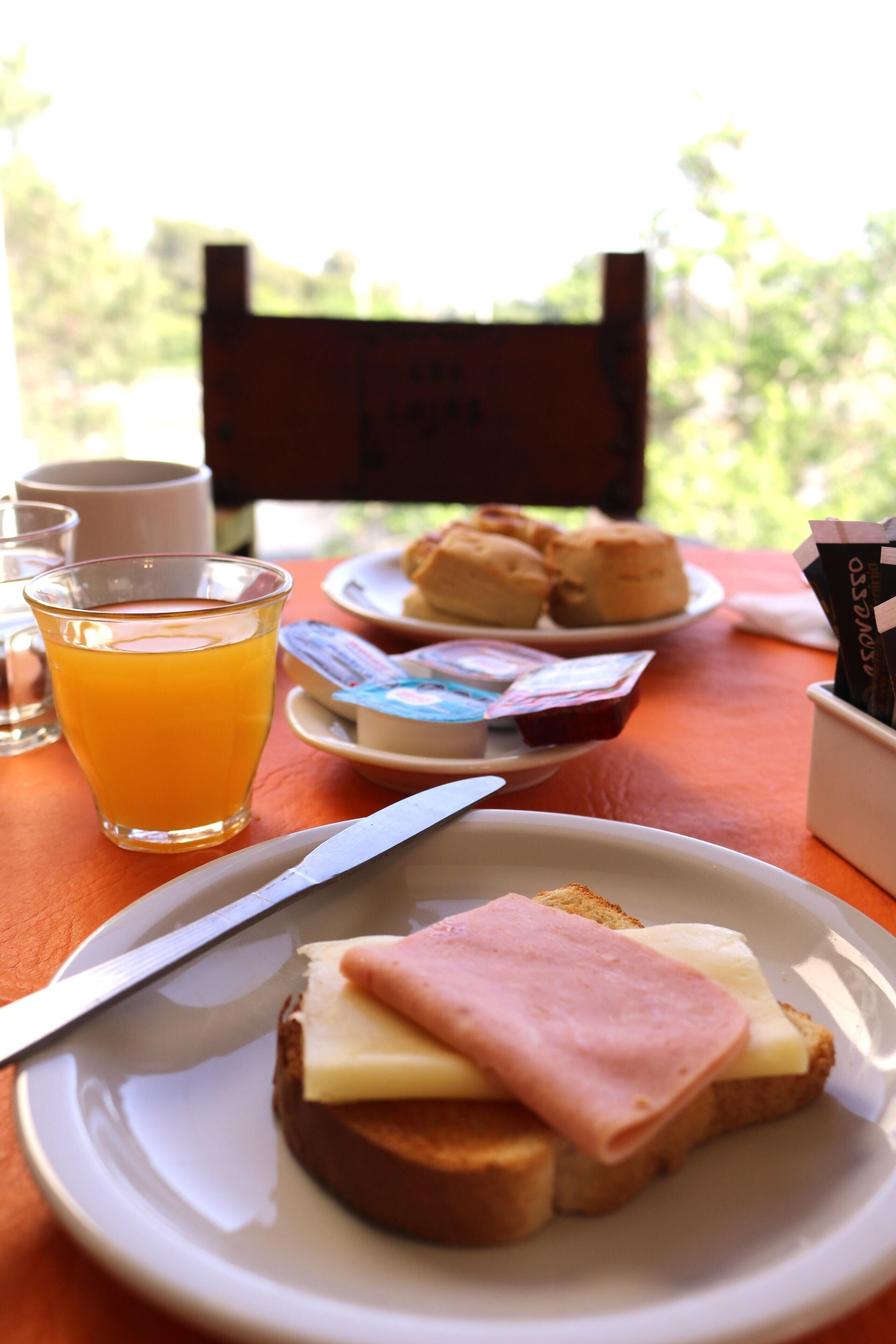 A breakfast setting with a plate of toast, ham, and cheese, a glass of orange juice, and a plate of pastries.