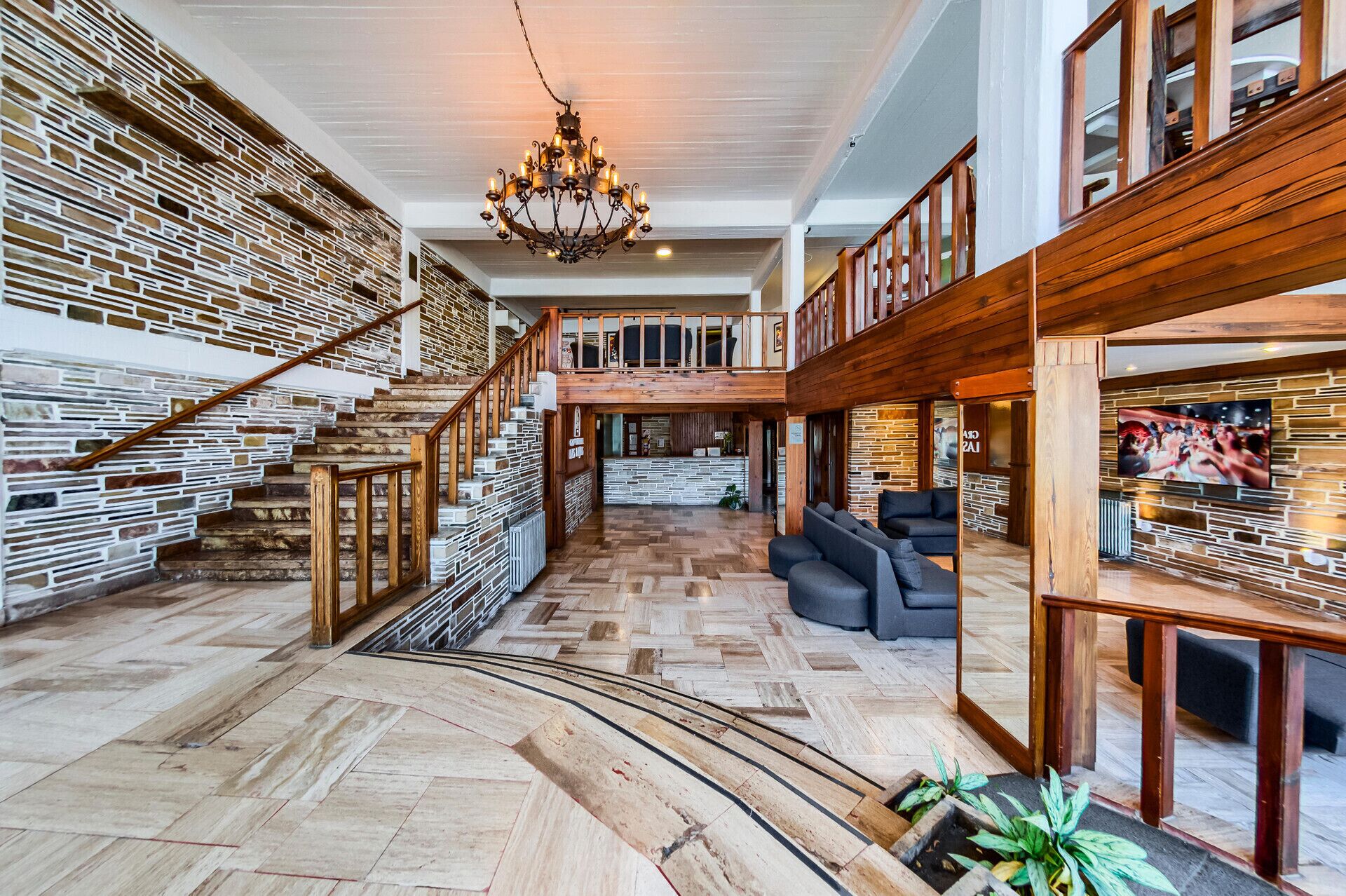 A spacious interior with a wooden staircase, a chandelier, and a seating area with a television.