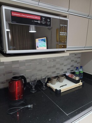 A kitchen with a stainless steel microwave, a kettle, wine glasses, and a tray with cups and bottled water. - Flat Super Luxo Verbo Divino (São Paulo)