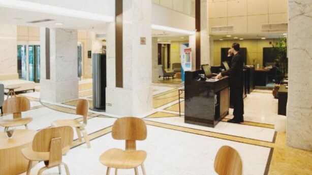 A modern hotel lobby with wooden furniture, a reception desk, and a unique ceiling sculpture.
