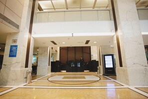 A hotel lobby with a reception desk, a digital information kiosk, and a marble floor. - Flat Super Luxo Verbo Divino (São Paulo)