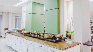 A buffet setup with multiple serving stations, a white cabinet with drawers, and a green accent wall.