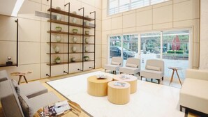 A modern interior with a high ceiling, a large window, and a seating area with round wooden tables and chairs.