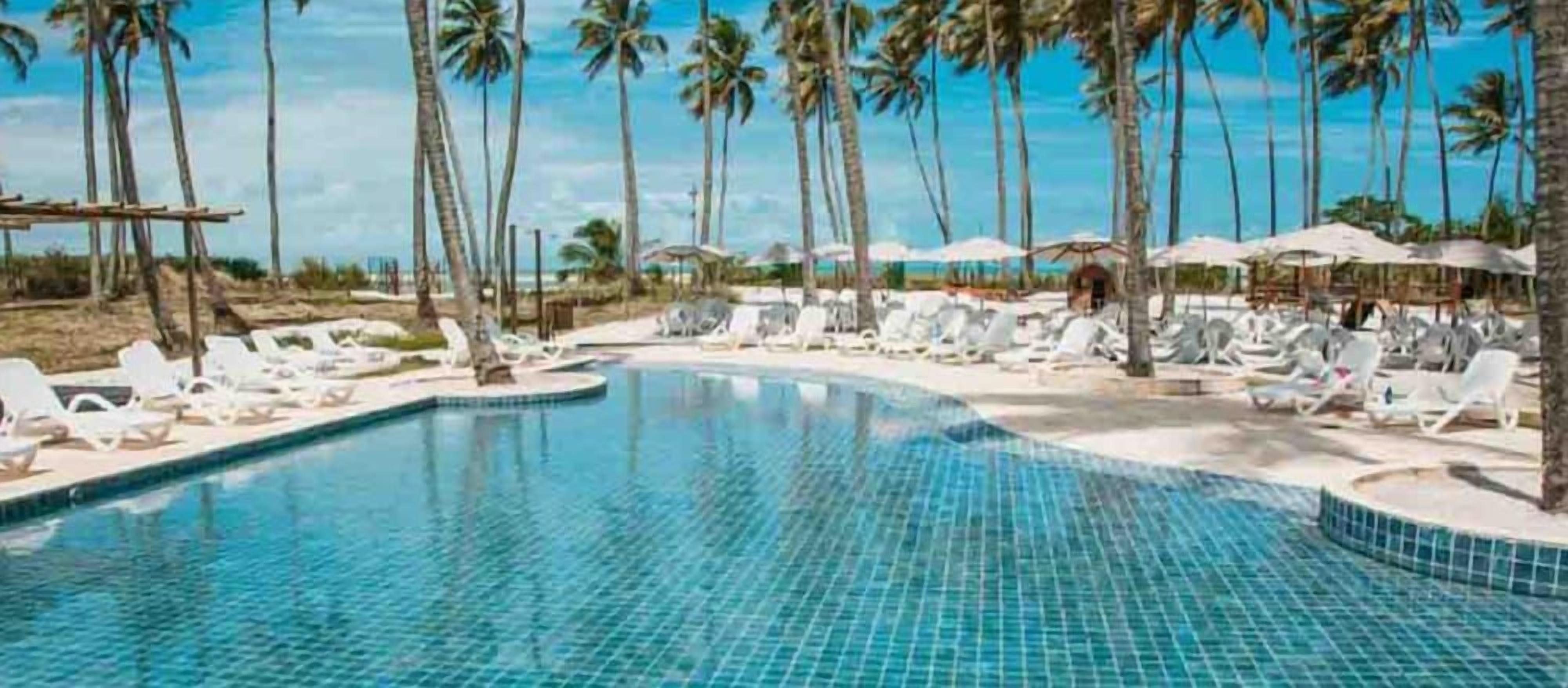 A swimming pool with lounge chairs and umbrellas, surrounded by palm trees.