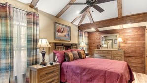 A bedroom with a wooden ceiling, a bed with a pink quilt, two bedside tables with lamps, a dresser, and a large mirror. - Stockyards Cowboy Lodge - 1/8 mi to Stockyards-Sleeps up to10-add 11 next door! (Fort Worth)