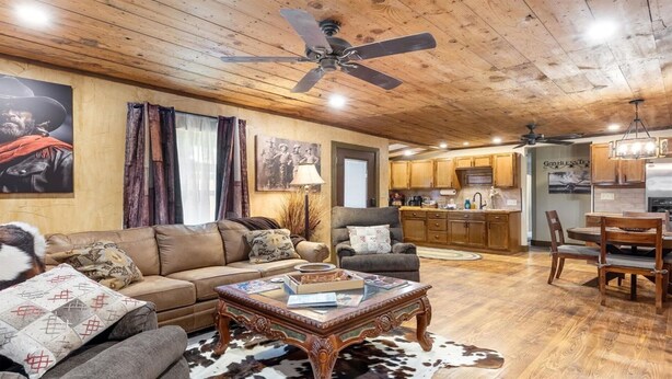 A cozy living room with a wooden ceiling, a sofa, a coffee table, and a dining area with a chandelier. - Stockyards Cowboy Lodge - 1/8 mi to Stockyards-Sleeps up to10-add 11 next door! (Fort Worth)