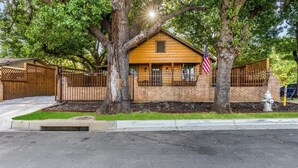 A two-story wooden house with a brick foundation, surrounded by trees and a wooden fence. - Stockyards Cowboy Lodge - 1/8 mi to Stockyards-Sleeps up to10-add 11 next door! (Fort Worth)
