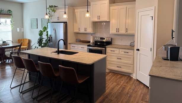 A modern kitchen with white cabinets, a central island with bar stools, a stainless steel refrigerator, and a black stove.