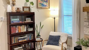 A cozy living room with a wooden bookshelf, a comfortable armchair, a patterned rug, and a painting on the wall.