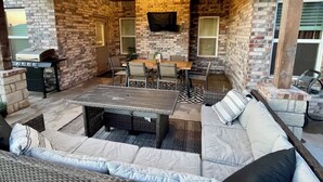 An outdoor patio with a brick wall, a grill, a table with chairs, and a sofa.