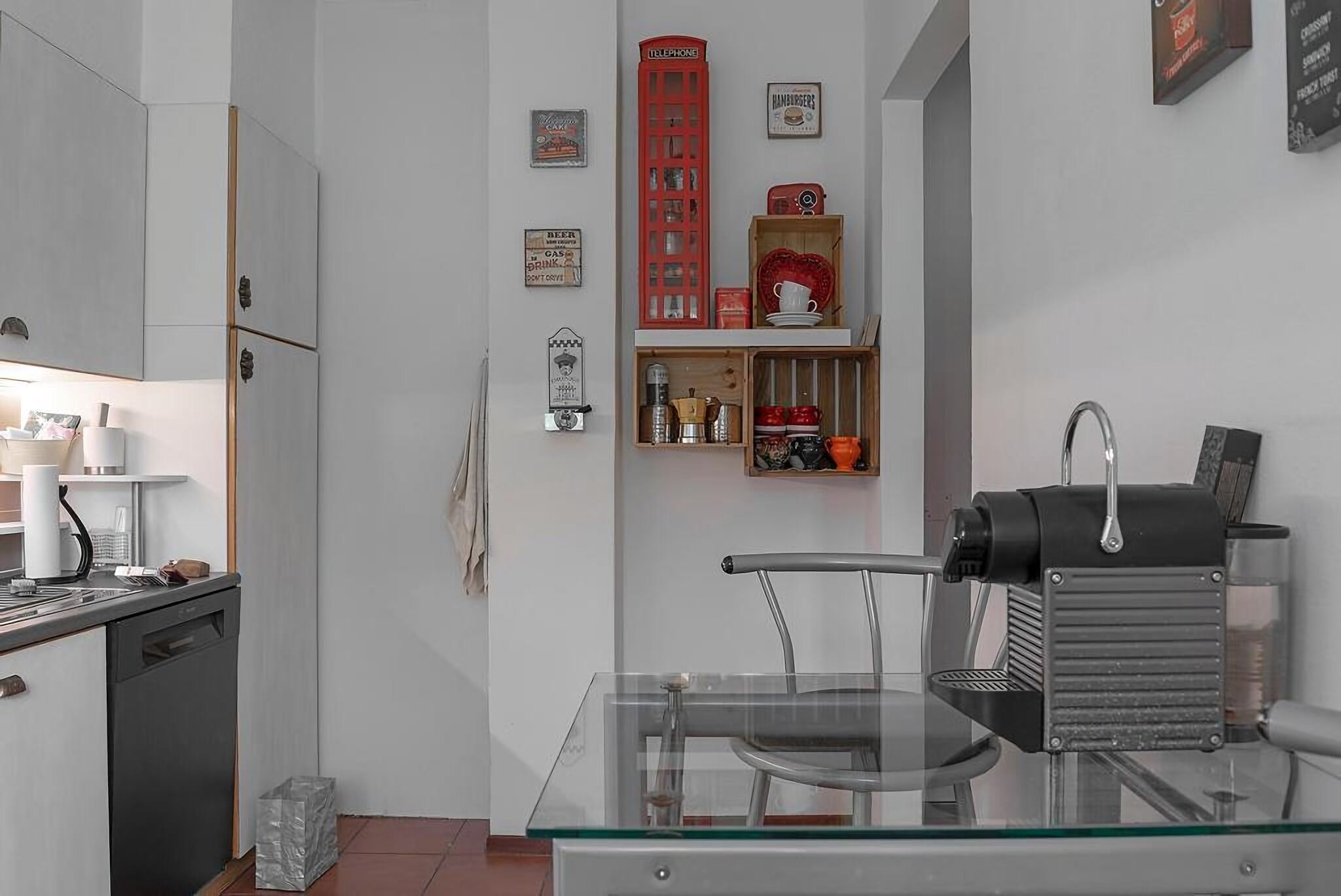 A compact kitchen with a dishwasher, a coffee machine, and a glass table.