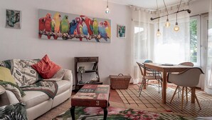 Un soggiorno con divano, tavolino da caffè, tavolo da pranzo con sedie e un quadro con uccelli colorati appeso al muro.