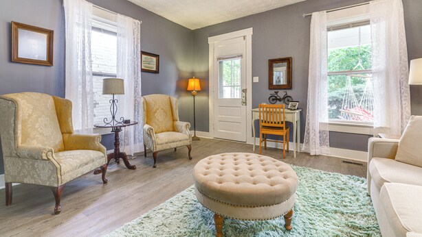 A living room with two armchairs, a round ottoman, a lamp, and a door leading to another room. - Dog-Friendly Dayton Home Near Downtown + Hospitals (Dayton)