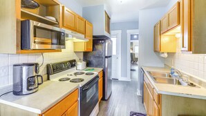 A compact kitchen with wooden cabinets, a stainless steel microwave, a toaster, a stove, and a refrigerator. - Dog-Friendly Dayton Home Near Downtown + Hospitals (Dayton)