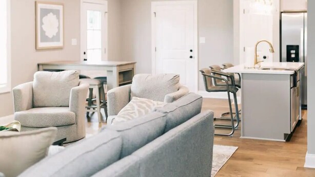 A modern living room with a grey sofa, a ceiling fan, and a kitchen area with a fridge and sink. - Cozy, Clean Home for Family or Friends (Bowling Green)