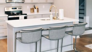 A modern kitchen with a central island, stainless steel appliances, and a bar stool seating area. - Cozy, Clean Home for Family or Friends (Bowling Green)