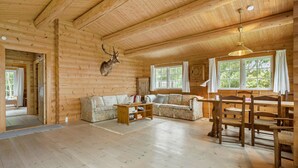 L’intérieur d’une cabane en rondins, avec un canapé, une table à manger, des chaises, une tête de cerf accrochée au mur et de grandes fenêtres.