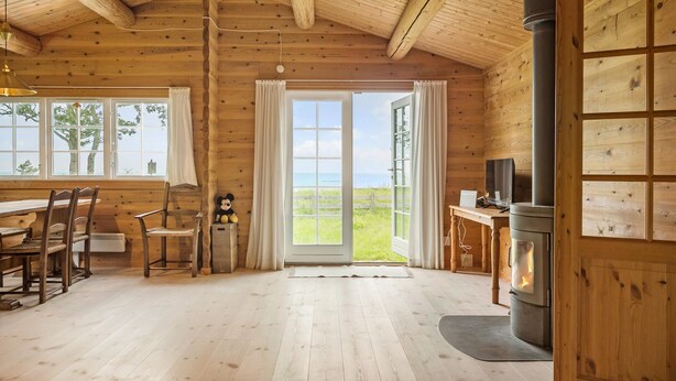 L’intérieur chaleureux d’un chalet avec des murs en bois, une grande fenêtre offrant une belle vue, un coin repas avec des chaises et une cheminée.