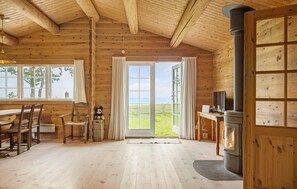 A cozy cabin interior with wooden walls, a large window with a view, a dining area with chairs, and a fireplace. - 3 bedroom stunning home in Gilleleje (Gilleleje)