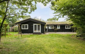 A black wooden cabin with a porch and a swing set in a grassy yard. - 3 bedroom stunning home in Gilleleje (Gilleleje)