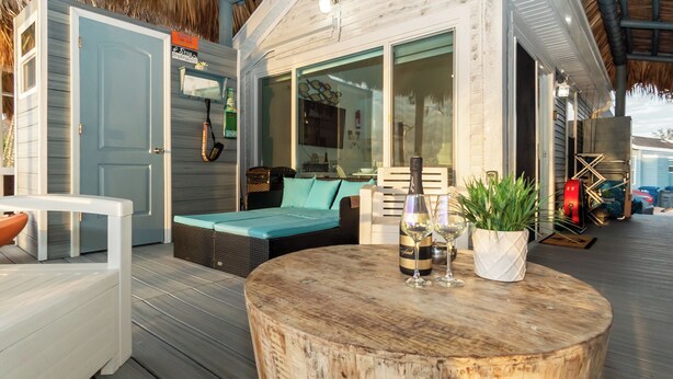 Een houten terras met een ronde tafel, een rieten bank en een bloempot.