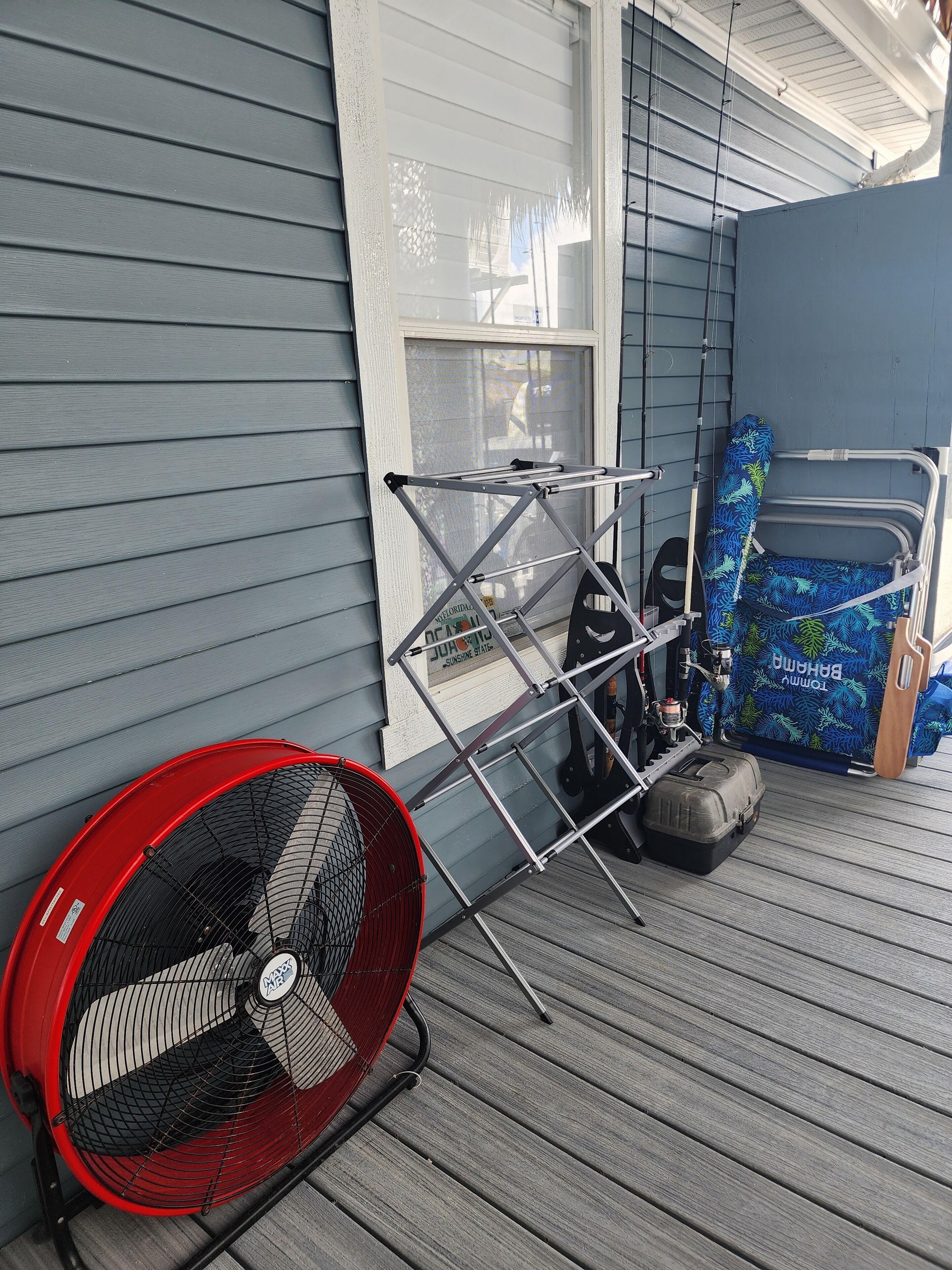 A red fan, a metal rack, and a blue chair on a wooden deck.
