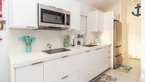 Een moderne keuken met witte kasten, een roestvrijstalen magnetron, een spoelbak en een koelkast. Op het aanrecht staan keukengerei en een blender.