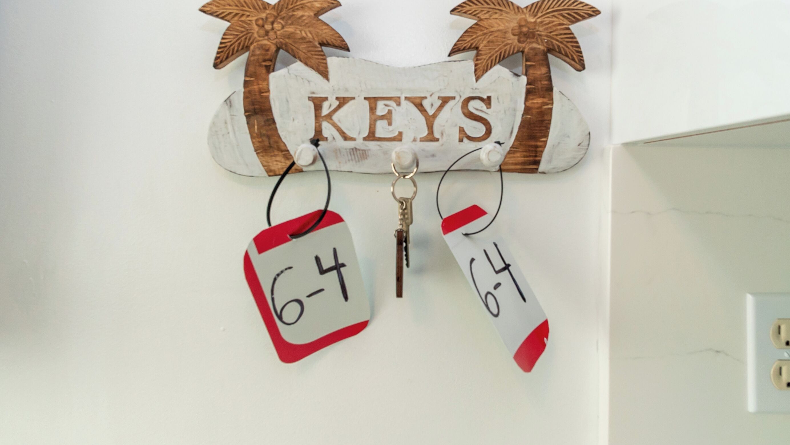 Een wandbord met de tekst 'KEYS' en daaronder twee labels, elk met het nummer '64' erop.