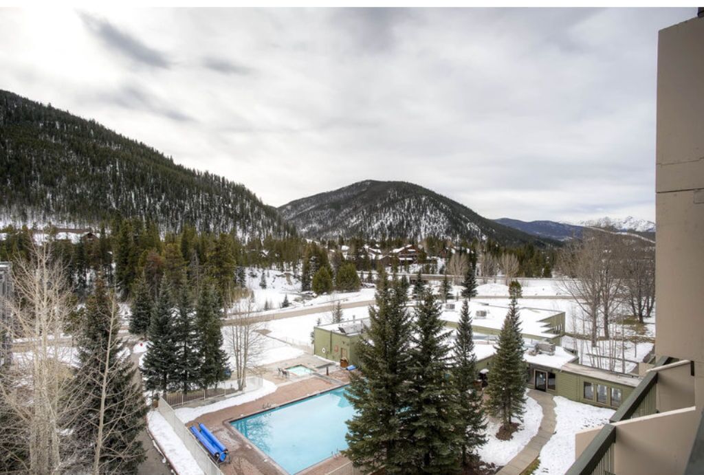 Zona residencial con piscina, telesilla y vistas a montañas nevadas.