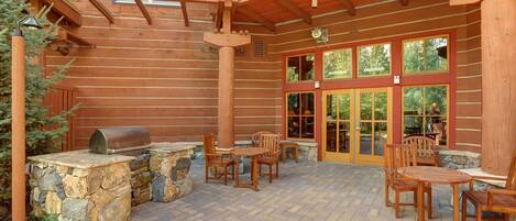 A wooden cabin with a stone fireplace, outdoor seating, and large windows.