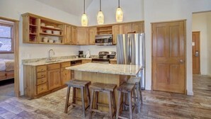 Une cuisine avec des meubles en bois, un îlot central doté de tabourets, un réfrigérateur en acier inoxydable et des luminaires suspendus.