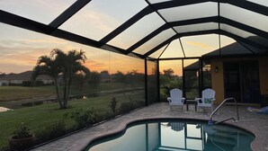 Ein überdachter Außenpool mit Sonnenuntergangsblick, eine Terrasse mit Stühlen und ein kleiner Garten.