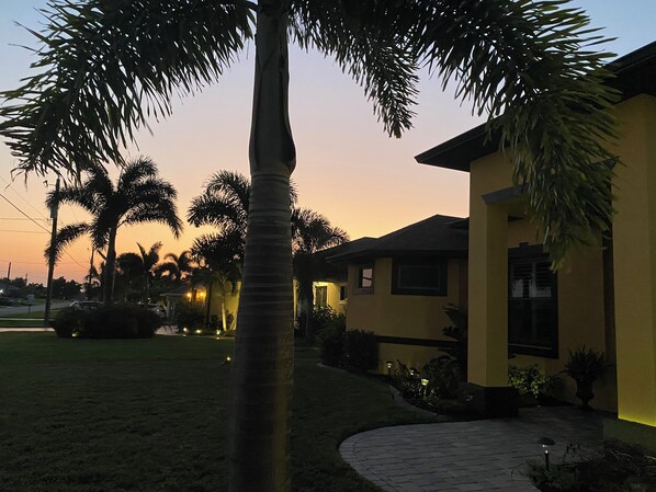 A residential area with a house, palm trees, and a paved pathway.