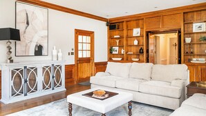 Un salon avec un canapé beige, un pouf blanc et un meuble en bois doté d’étagères.