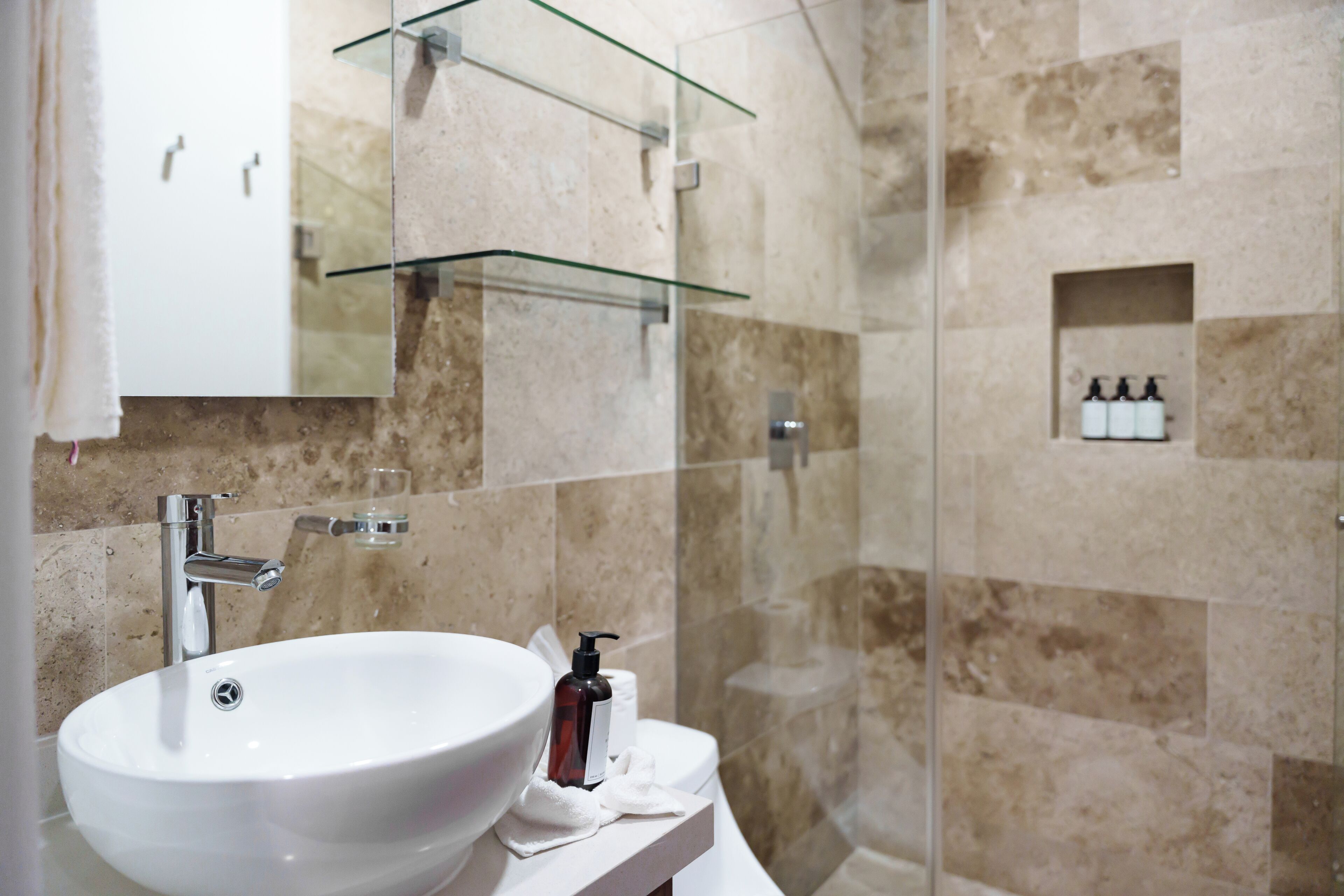Un baño con un lavabo blanco, repisas de vidrio y una zona de ducha.
