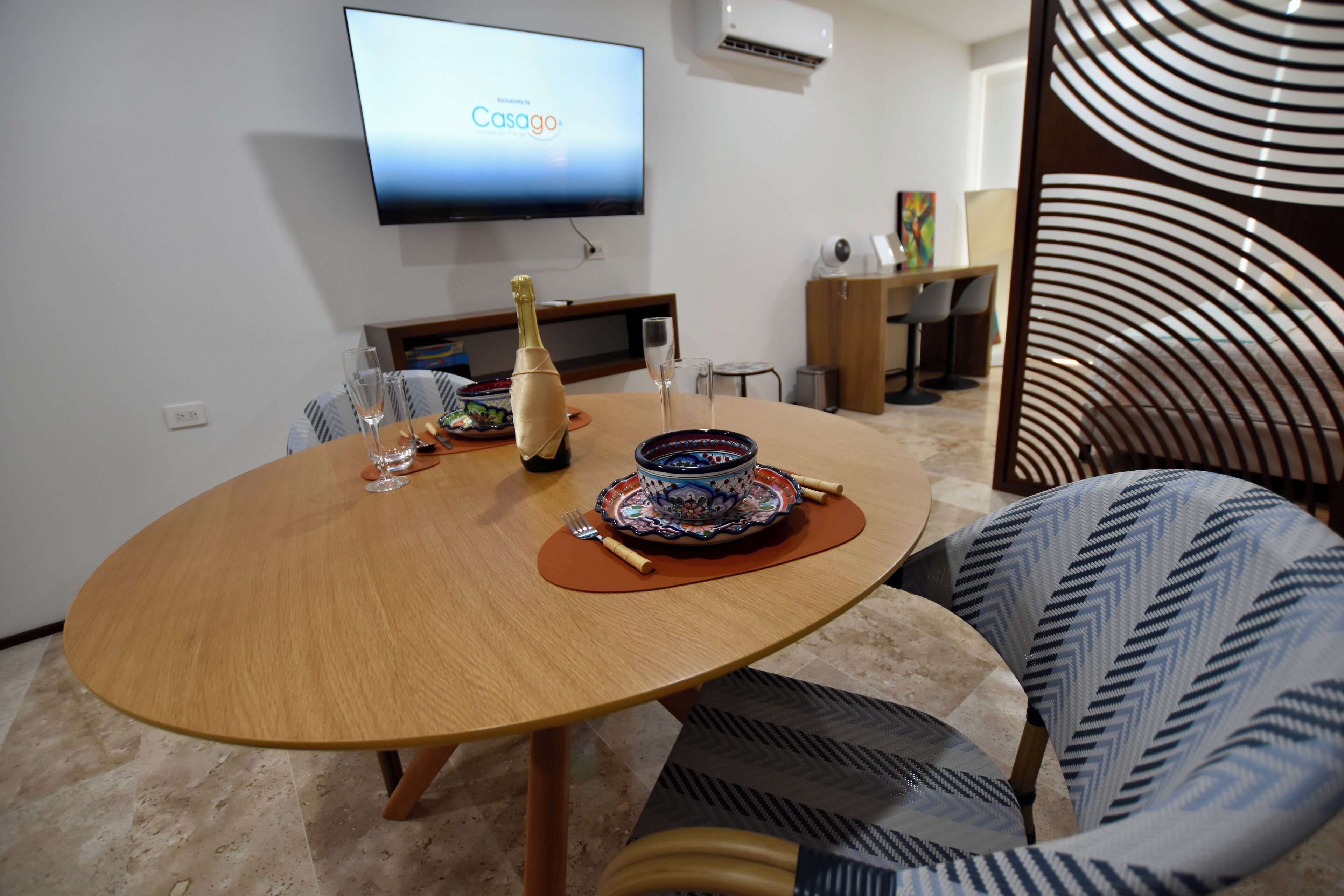 A modern dining area with a wooden table, chairs, and a television displaying 'Casago'.