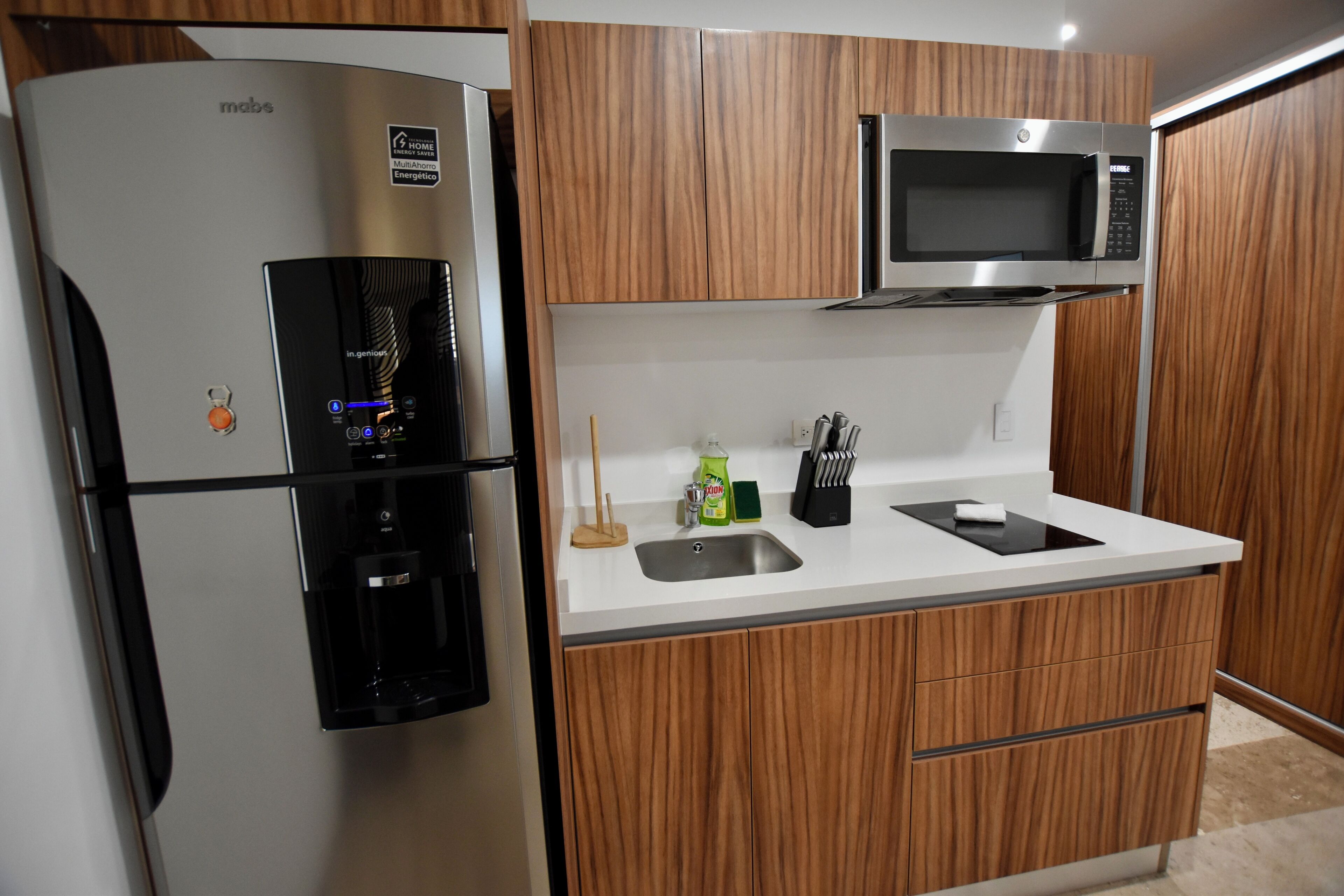 Una cocina compacta con un refrigerador de acero inoxidable, un microondas y armarios de madera.