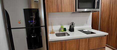Una cocina compacta con un refrigerador de acero inoxidable, un microondas y armarios de madera.