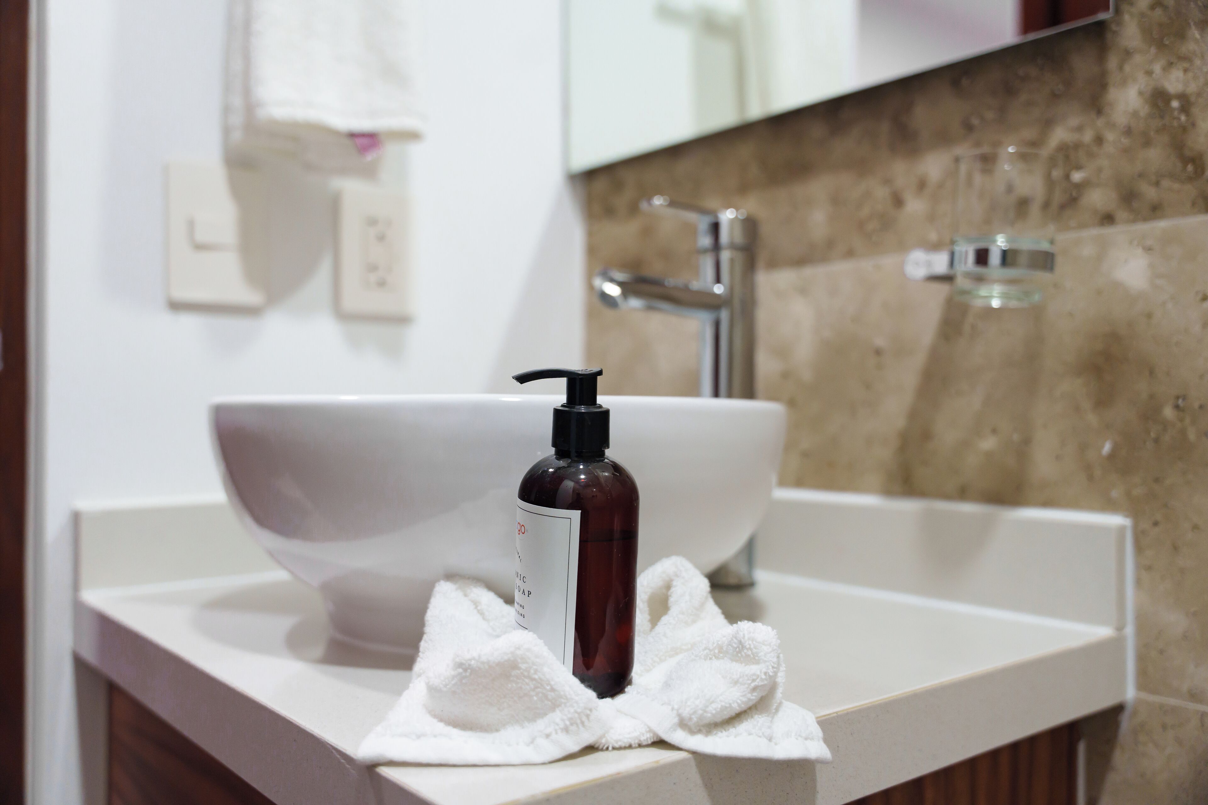 Une salle de bain avec un lavabo blanc, un flacon de savon liquide et une serviette blanche posée sur le comptoir.