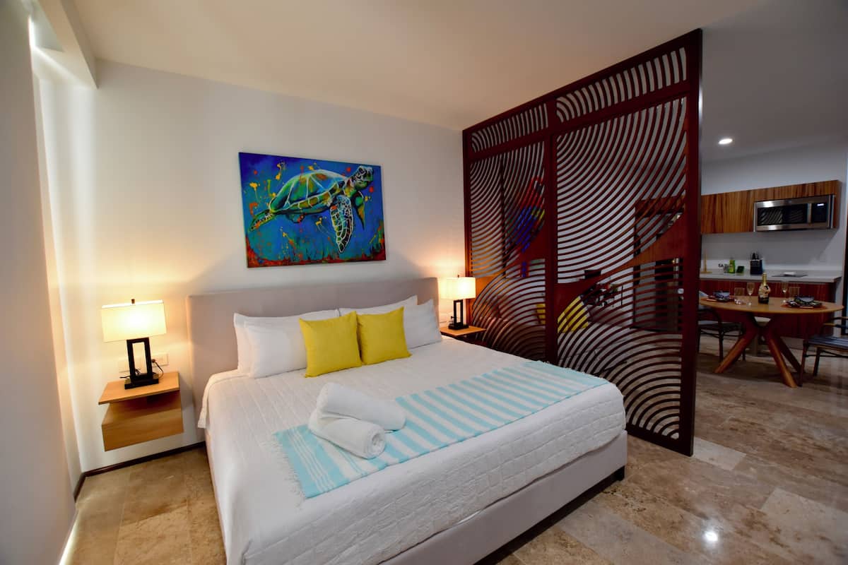 Hotelkamer met een bed, twee bedlampen, een schilderij van een zeeschildpad, een houten scheidingswand, een bureau en een stoel.