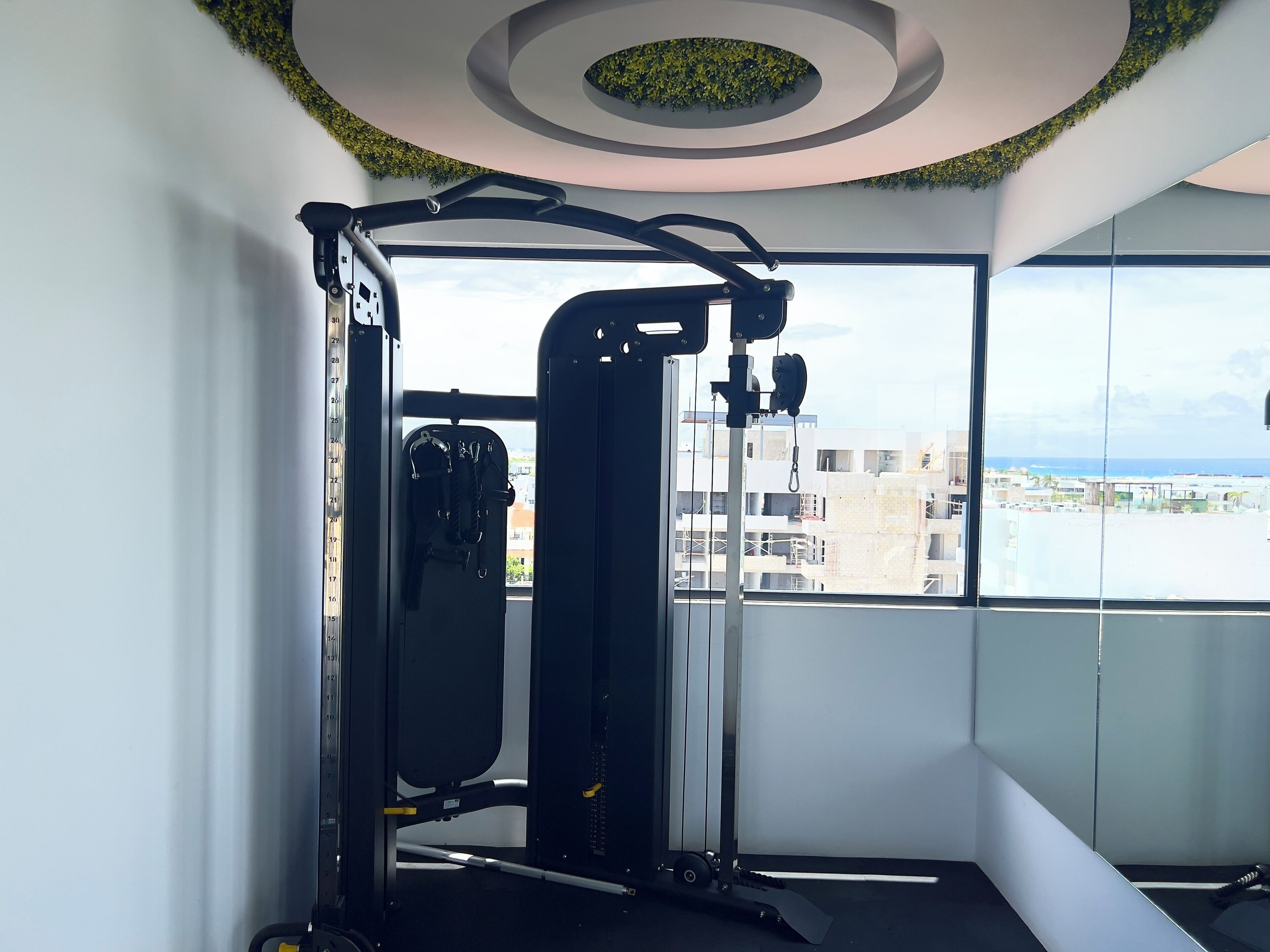 Une salle de sport équipée d’une barre de traction et d’appareils de musculation, de grandes fenêtres offrant une vue sur la ville et d’un plafond au design circulaire.