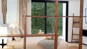 Ein modernes Schlafzimmer mit großem Fenster, einem Bett mit Kissen, einem Nachttisch und einer Holzleiter an der Wand.