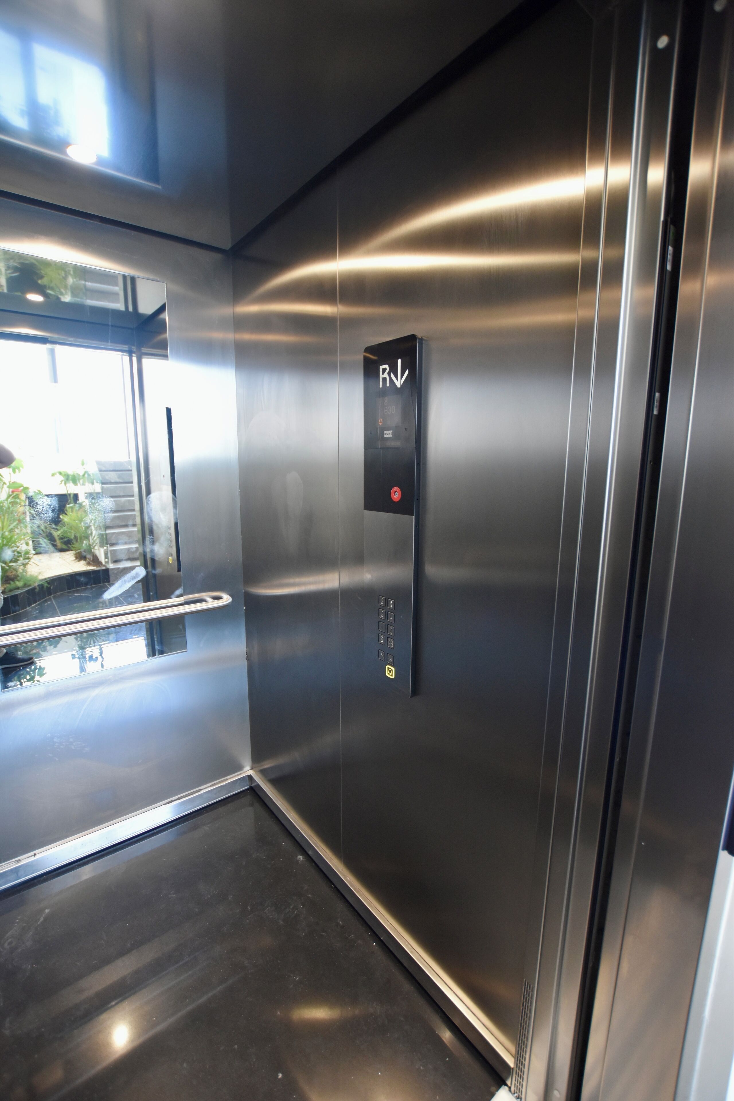 Um elevador moderno com painel de controle, paredes metálicas e porta de vidro.