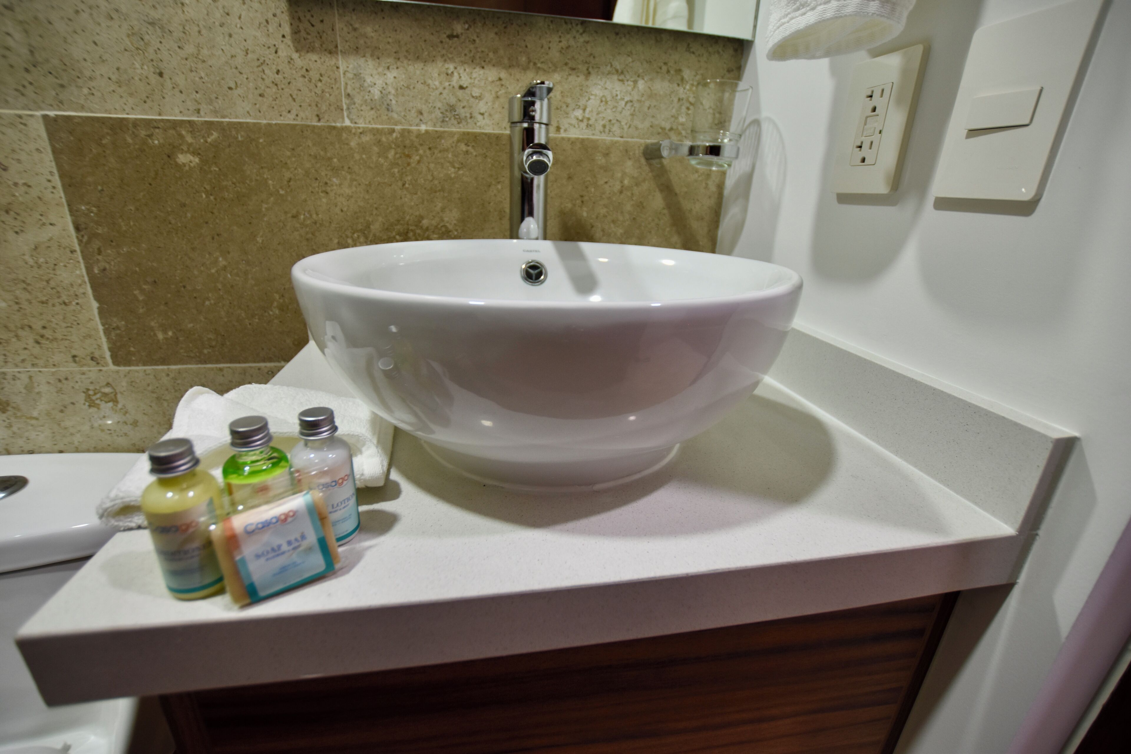 Un bagno con un lavandino bianco, uno specchio e un portascopevoli. Sul mobile ci sono tre flaconi di sapone.