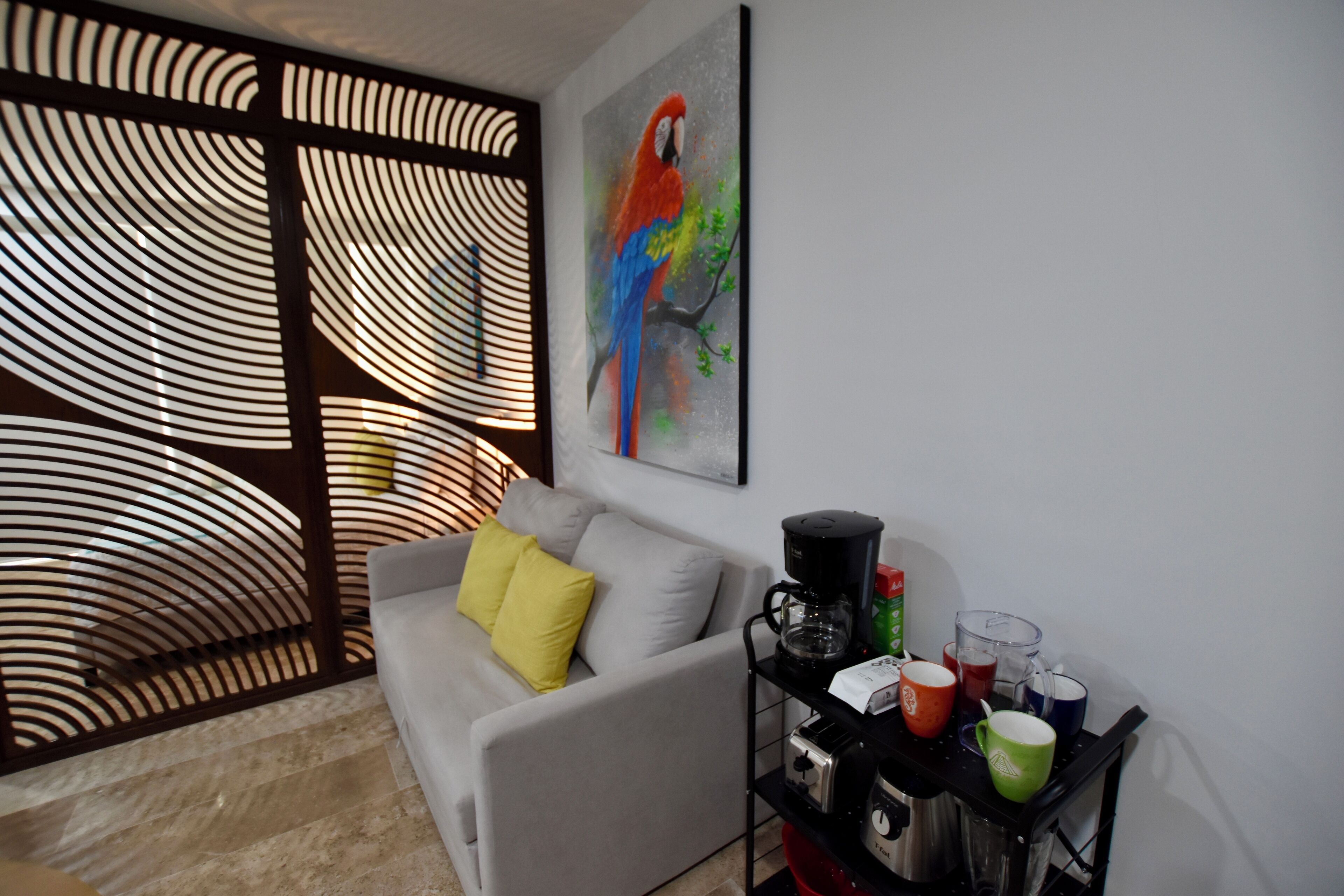 A modern living room with a grey sofa, yellow pillow, and a coffee machine on a black stand.