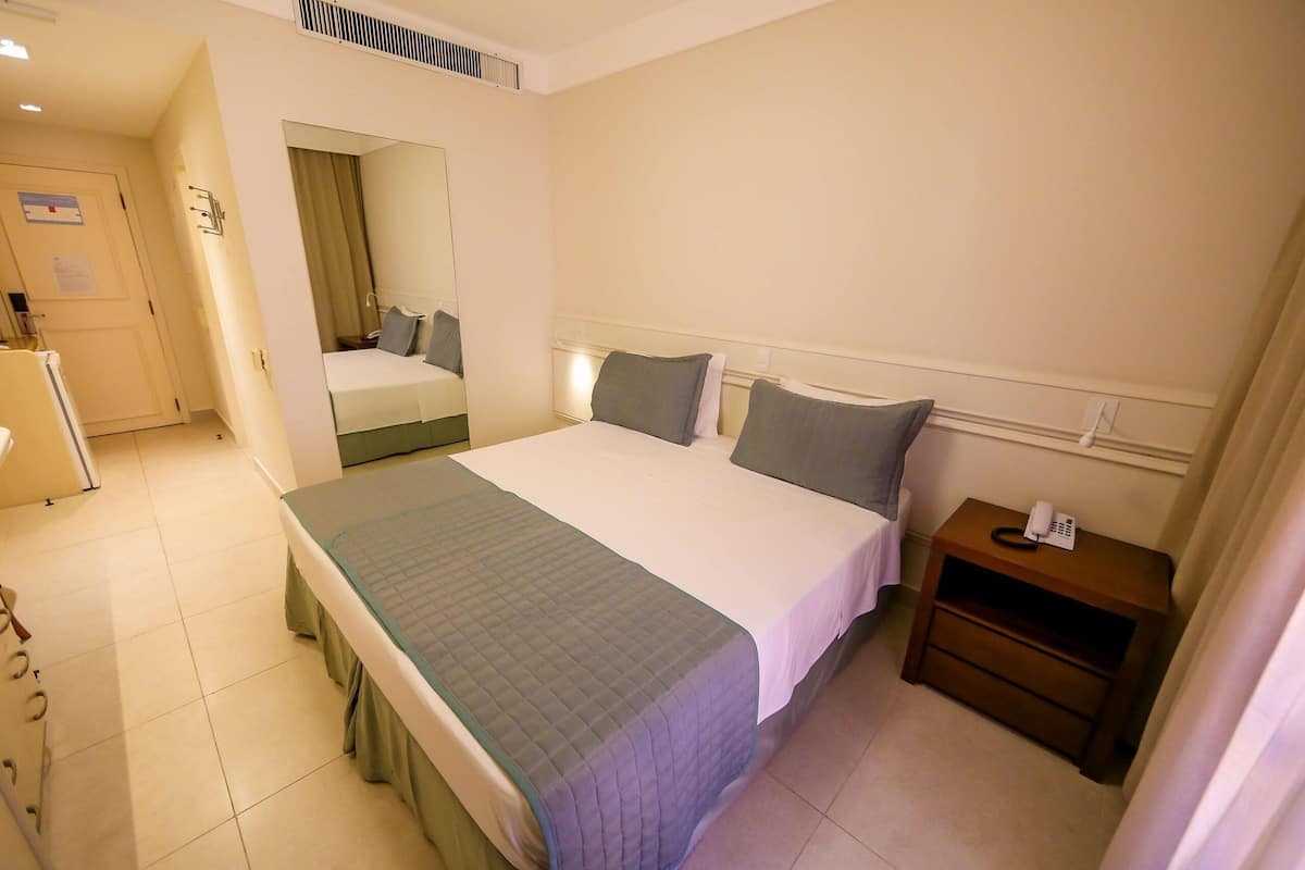 Una habitación de hotel con cama, mesita de noche y espejo.