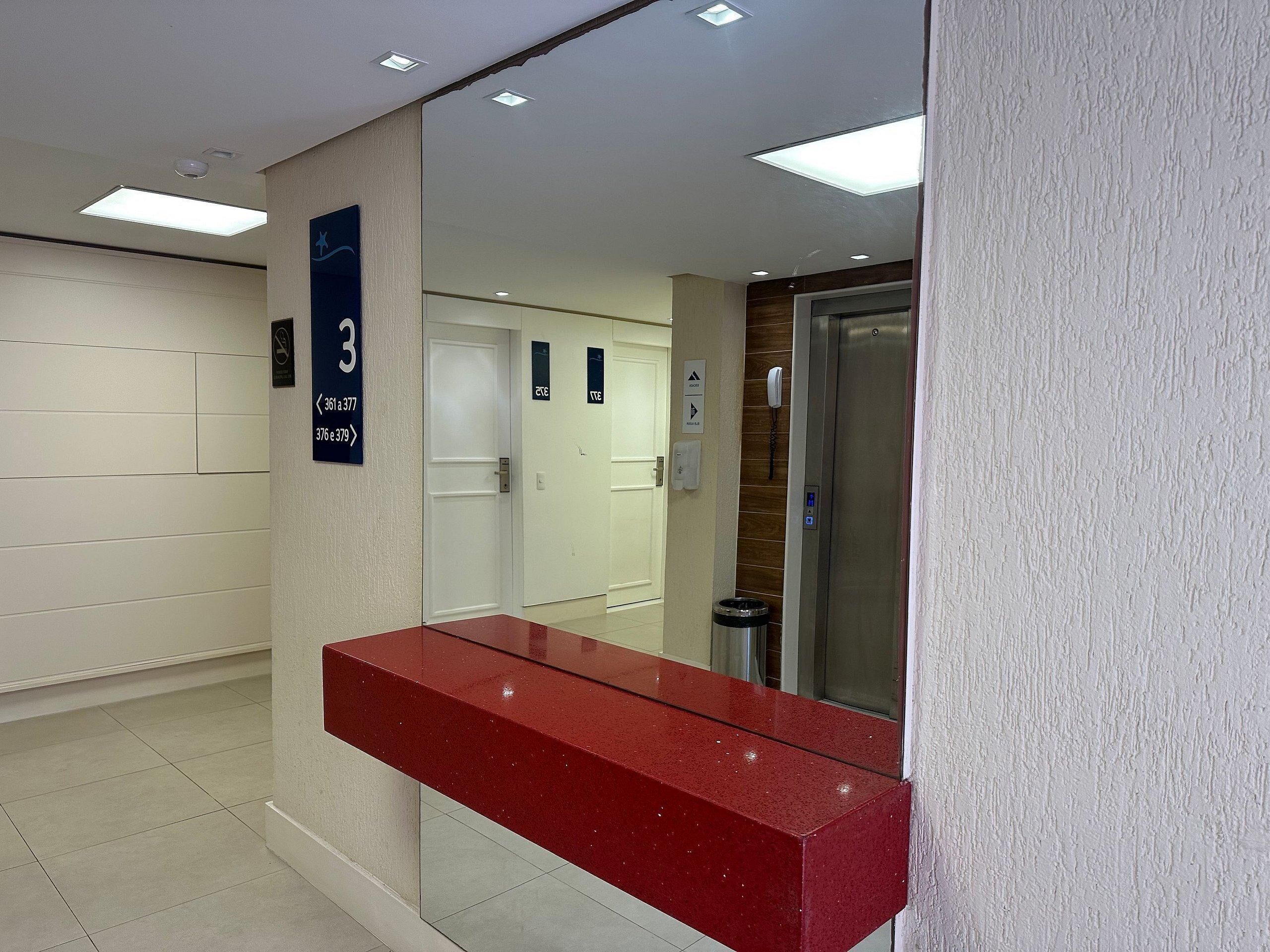 Zona de recepción de un hotel con un mostrador rojo, un cartel con el número 3 y un ascensor.
