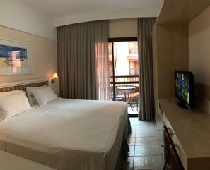 A hotel room with a large bed, a television, a balcony with a table and chairs, and a view of the outside. - Jurerê Beach Village é Destino Floripa (Florianópolis)