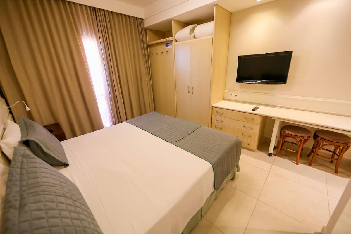 Habitación de hotel con cama, escritorio, televisor y armario.