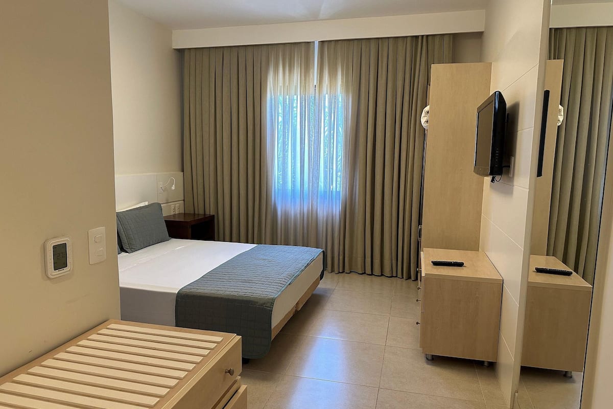 Una habitación de hotel con cama, escritorio, televisión y ventana con cortinas.